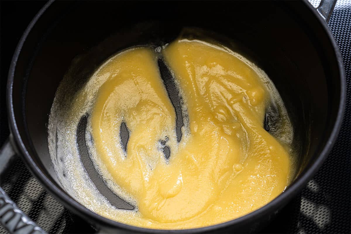 Image of roux being made in a pot, showing butter melting and flour being whisked together to form a smooth paste.