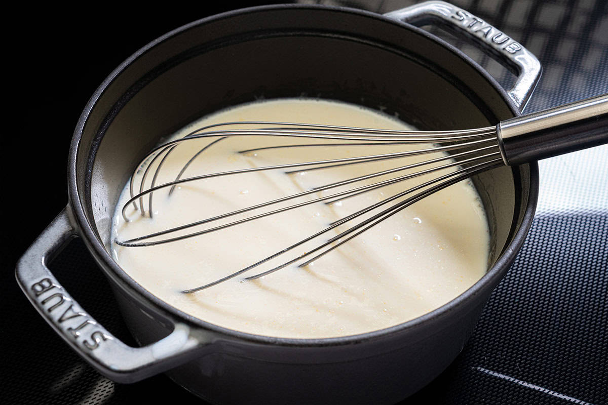 Image of milk being added to the roux in a pot, showing the process of creating a smooth and creamy bechamel sauce.
