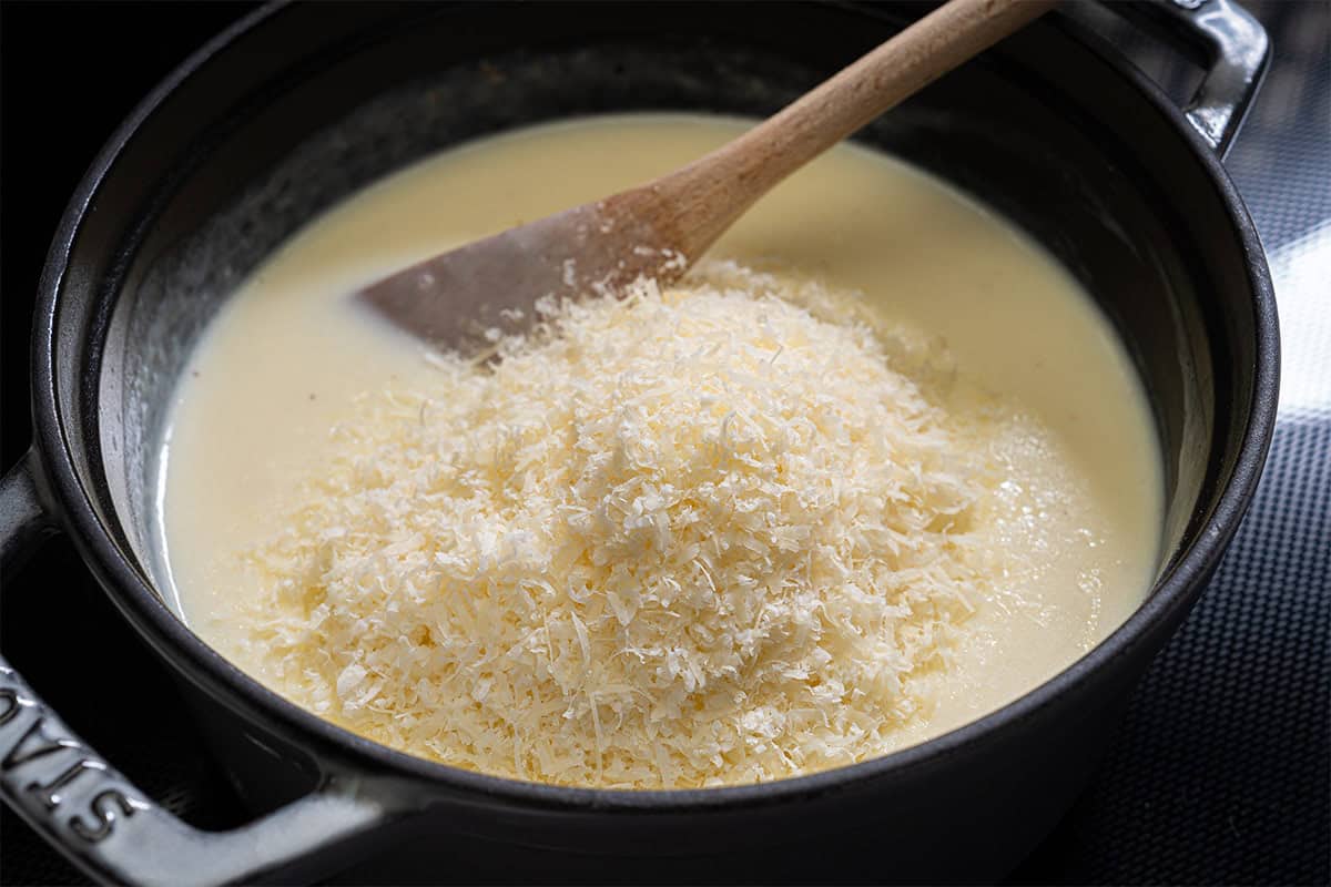 Image of parmesan being added to the bechamel showing the process of creating a smooth and creamy bechamel sauce.
