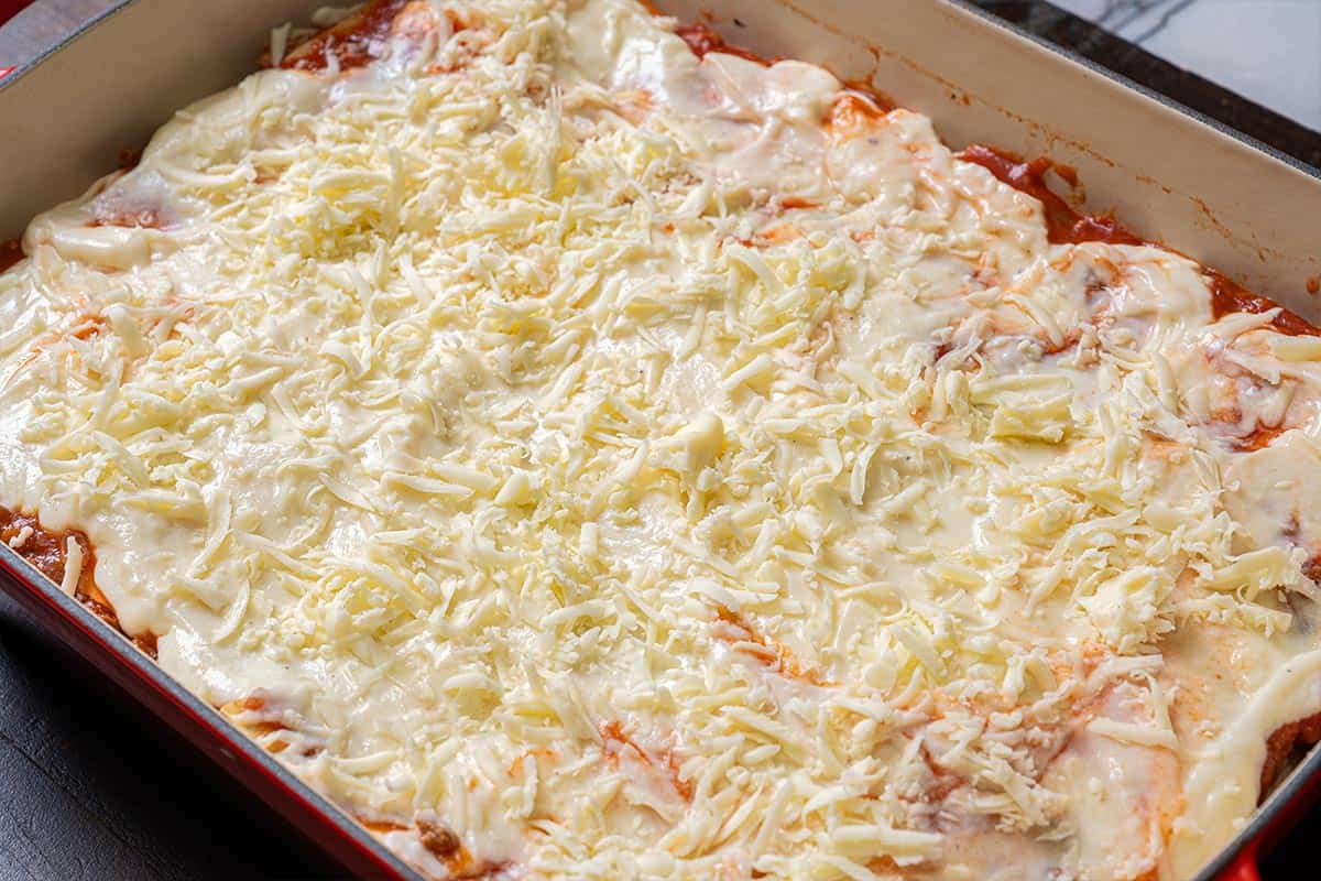 Image of the final layer of lasagna being assembled, topped with mozzarella cheese and white sauce.