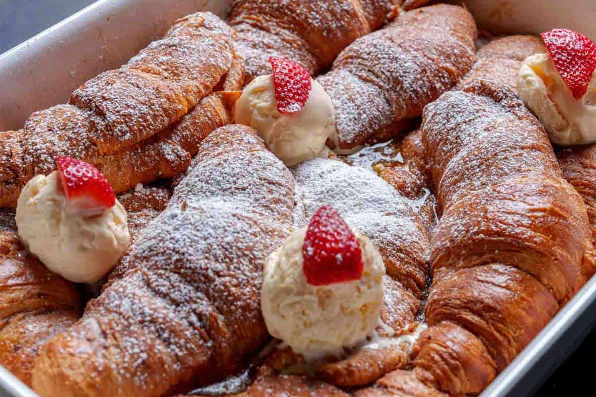 An image of the French toasts being taken out of the oven, coated with icing sugar and accompanied by a scoop of vanilla ice cream with half a strawberry on top, ready to be served.