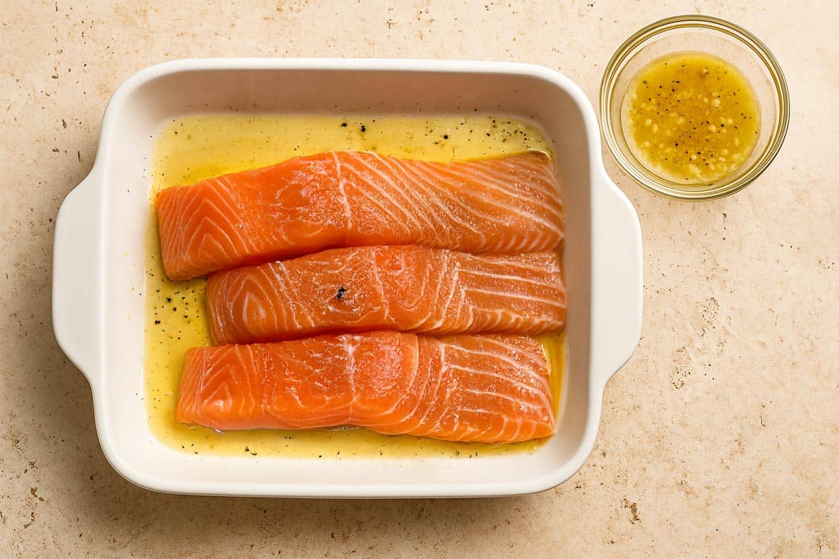 Marinated salmon fillets arranged in a white baking dish, coated with a golden lemon-garlic mixture.