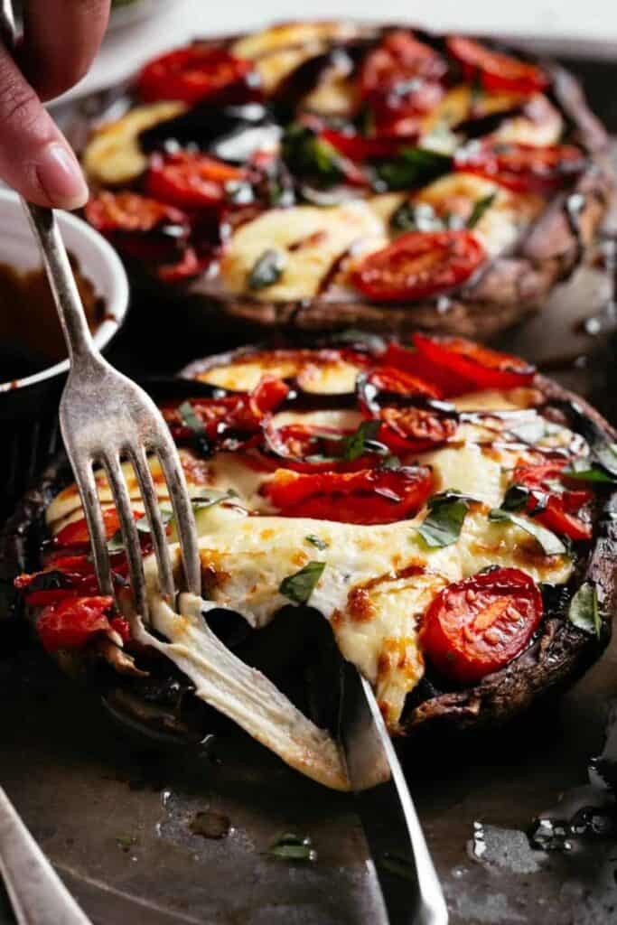 Hot and spicy Stuffed portobello being cut open with a knife and fork, the melted mozzarella stretching into strings between the cut. 