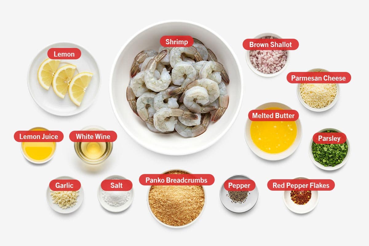 Top shot of ingredients: lemon, lemon juice, white wine, garlic, salt, panko breadcrumbs, pepper, shrimp, brown shallot, parmesan cheese, melted butter, red pepper flakes, and parsley.