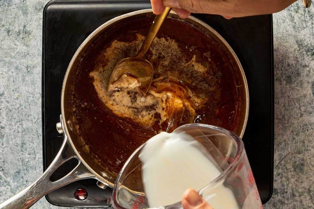 a pot sitting on a stove top with brown liquid inside and also what looks like corn starch and water being poured into it.