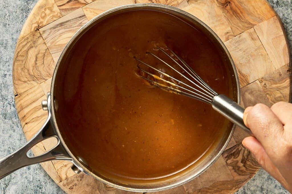 a light brown thick liquid inside a pot sitting on a stove top with a whisk inside striring the pot
