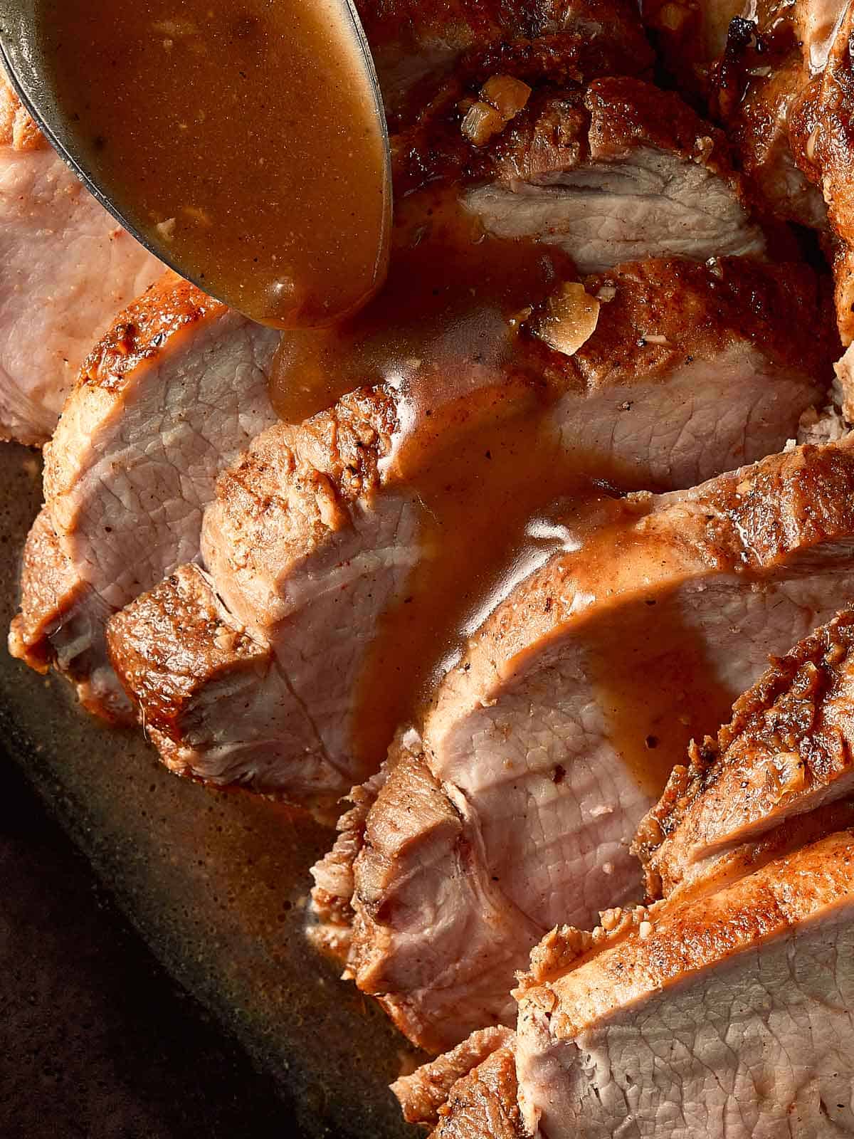 top down view of pork loin roast cut into half inch pieces in a log formation. fully cooked on the inside covered with gravy