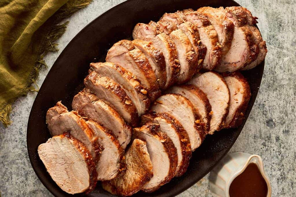 top down view of pork loin roast cut into half inch pieces in a log formation. fully cooked on the inside covered with gravy