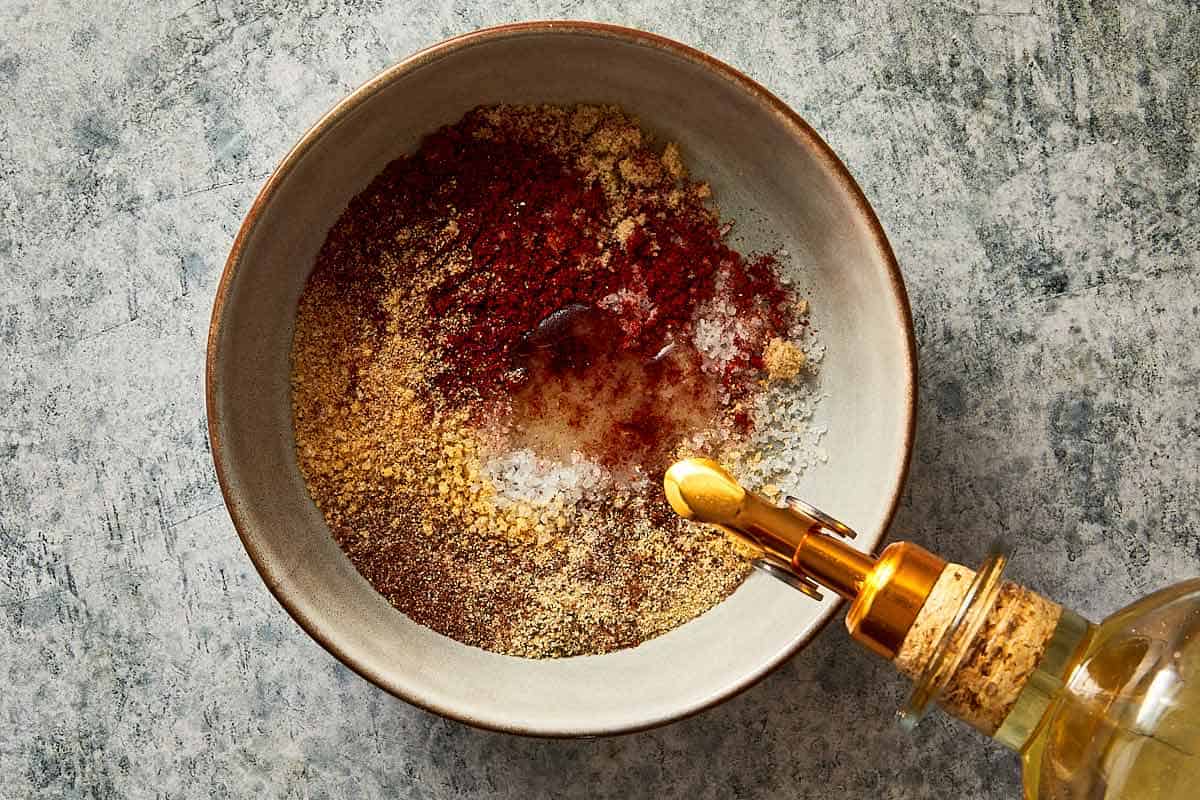 a top down view of a bowl filled with spiced and an oil bottle with a spout pouring liquid into the bowl