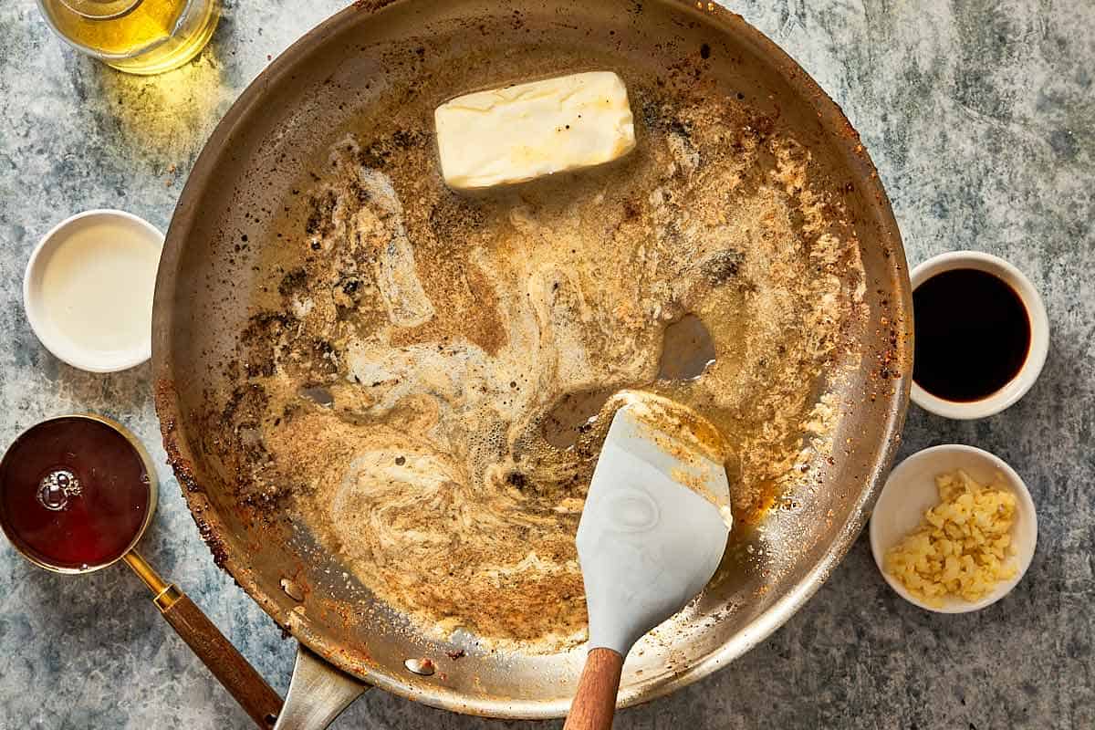 a top down shot of a frying pan with butter melting inside and a spatula mixing spices