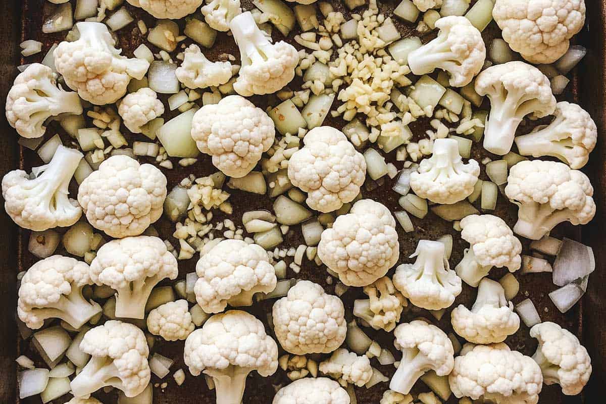 Cauliflower, mined garlic, and onion on a baking sheet.