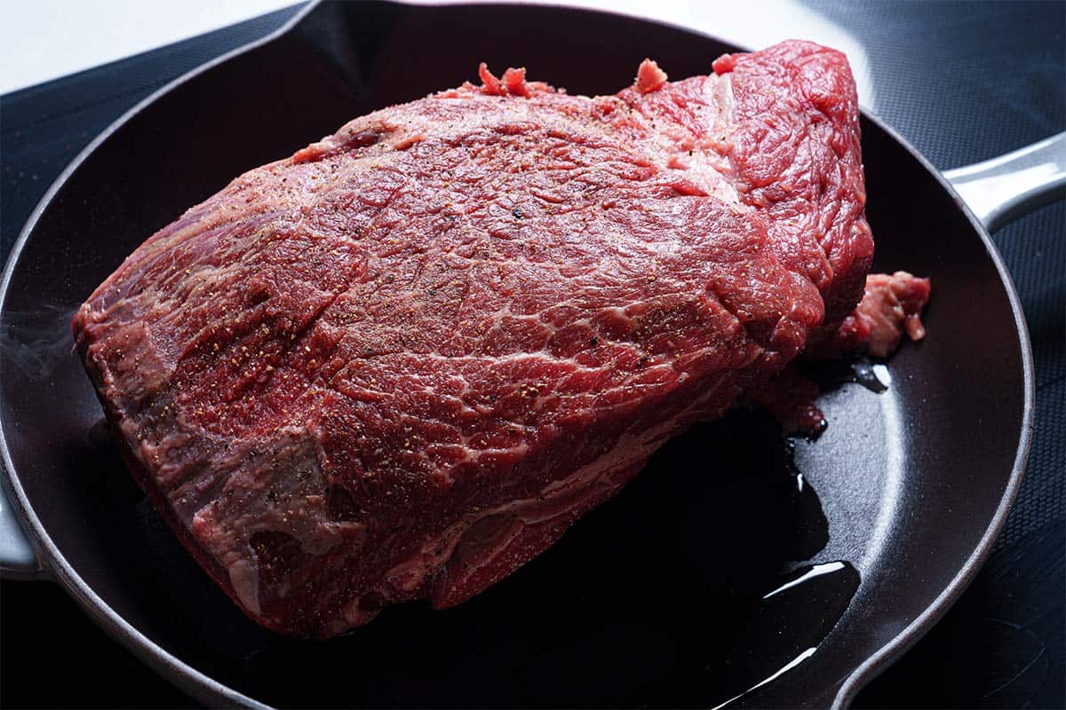 An image of the beef seasoned with salt and pepper being transferred to the skillet to be seared.