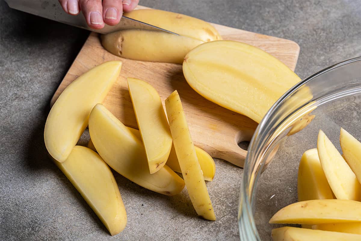 Hands are cutting the potatoes into halves, quarters, and then making them into wedges.