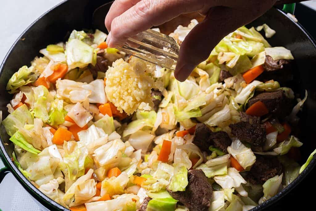 onions, carrots, celery cabbage. and garlic being sauted close up in a black pan