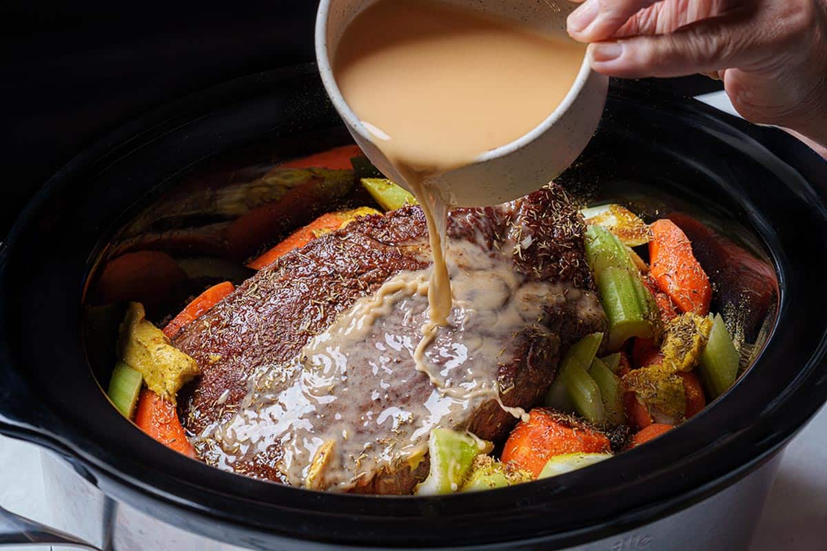 An image of the chuck beef being placed into the slow cooker while being coated in sauce.