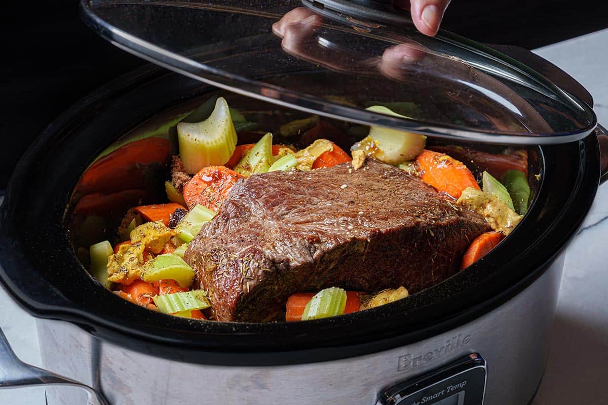 An image of the slow cooker being cooked on low for 8 hours to tenderize the meat and soften the vegetables.