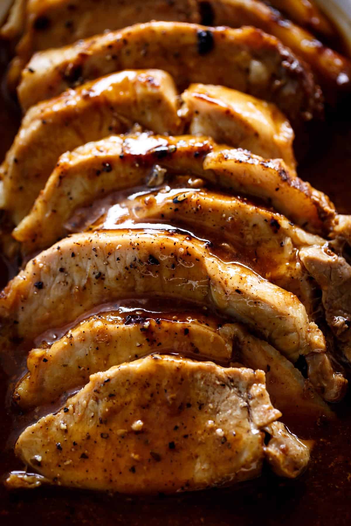 Sliced roast pork loin served on a platter, generously soaked in a rich, golden-brown sauce.