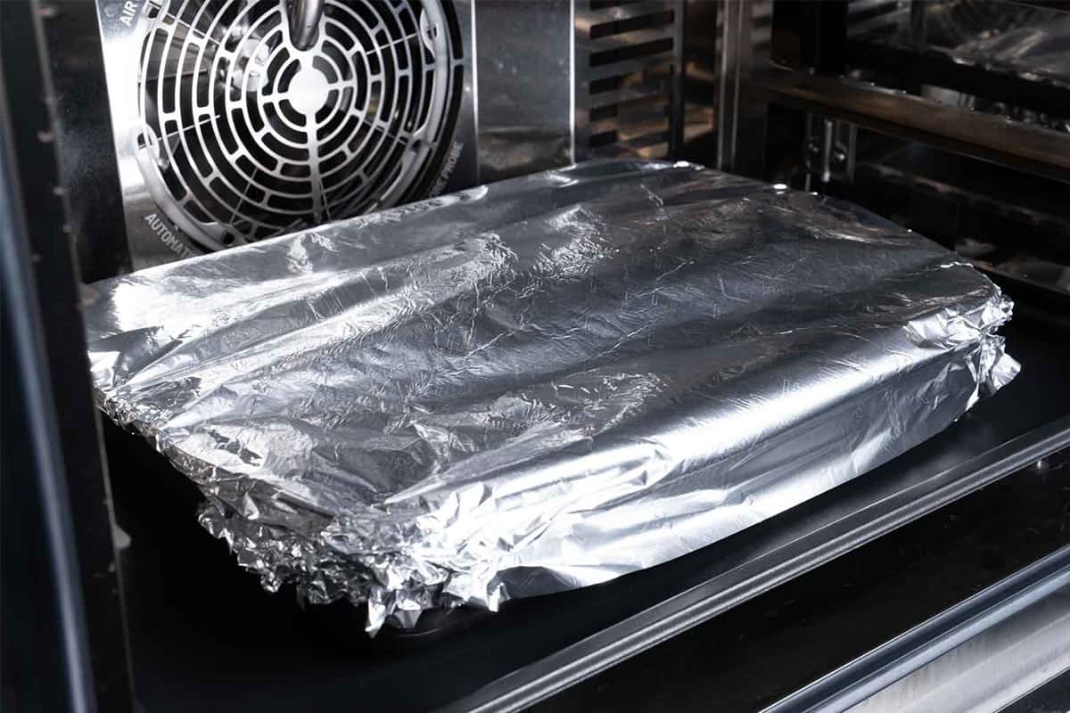 Image of the ribs being cooked in the oven covered with foil.
