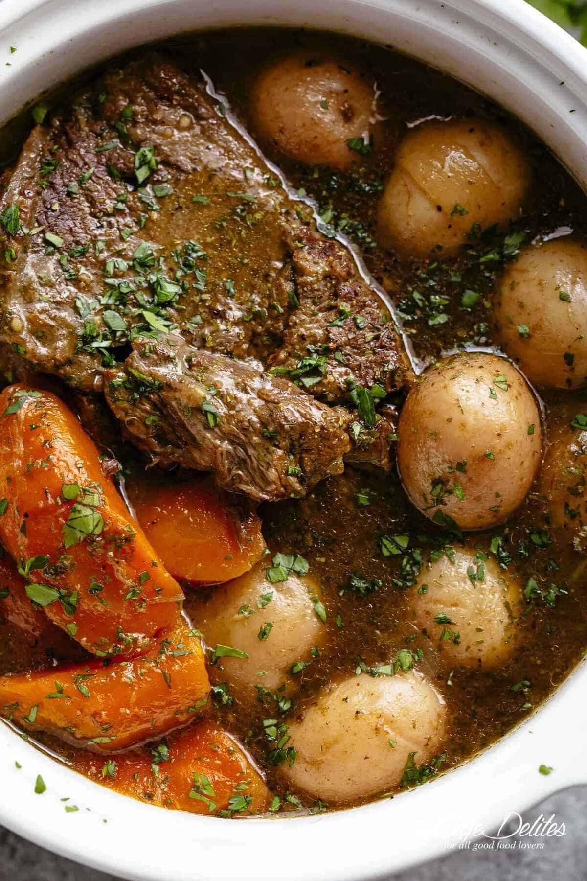 A close-up image of a tender piece of beef chuck, cooked in its own juices alongside potatoes and carrots.