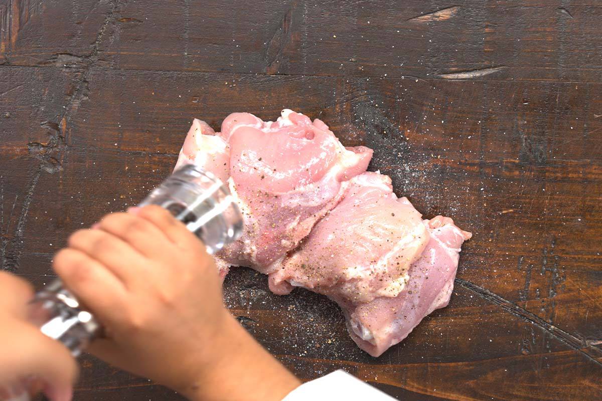 chicken thigh being seasoned with salt and pepper