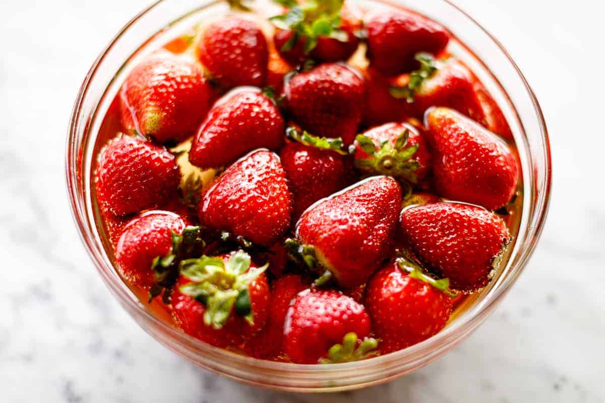 Top view of a glass bowl holding ripe strawberries soaking in alcohol. 