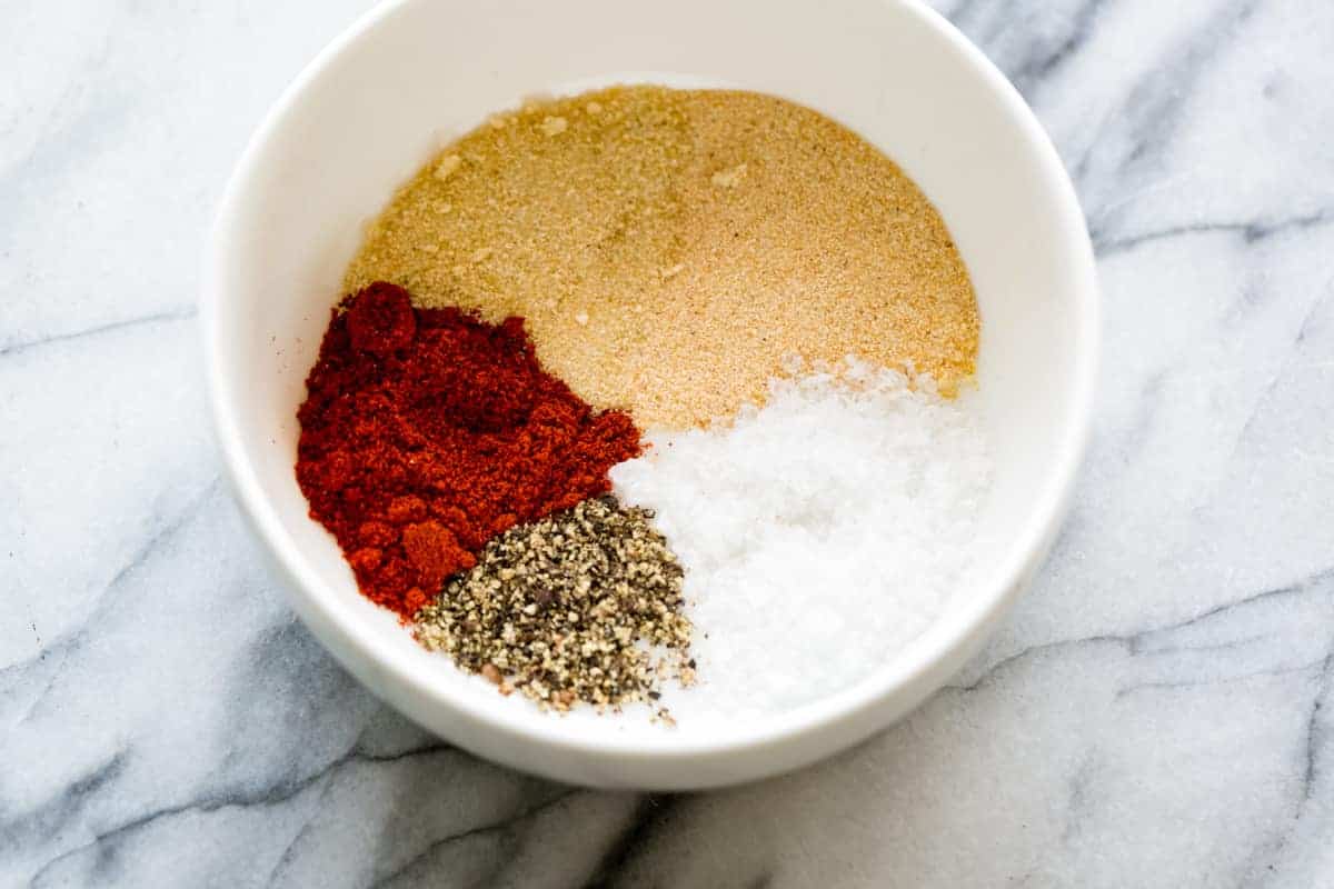White bowl filled with paprika, garlic powder, onion powder, salt, and pepper for seasoning chicken.