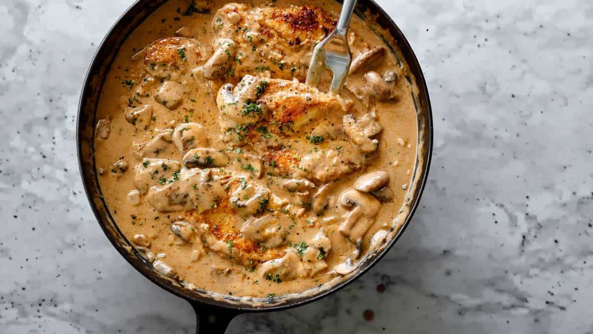 Golden seared chicken breasts simmering in a creamy mushroom stroganoff sauce in a skillet.