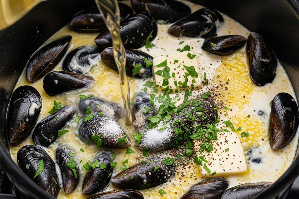 mussels, heavy cream, butter, chopped parsley, salt and pepper in a pot with white wine being poured.
