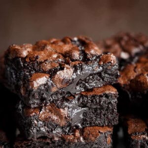 Side view of three slices of chocolate brownie stacked on top of each other. The brownies have a light brown top and dark, gooey interior.