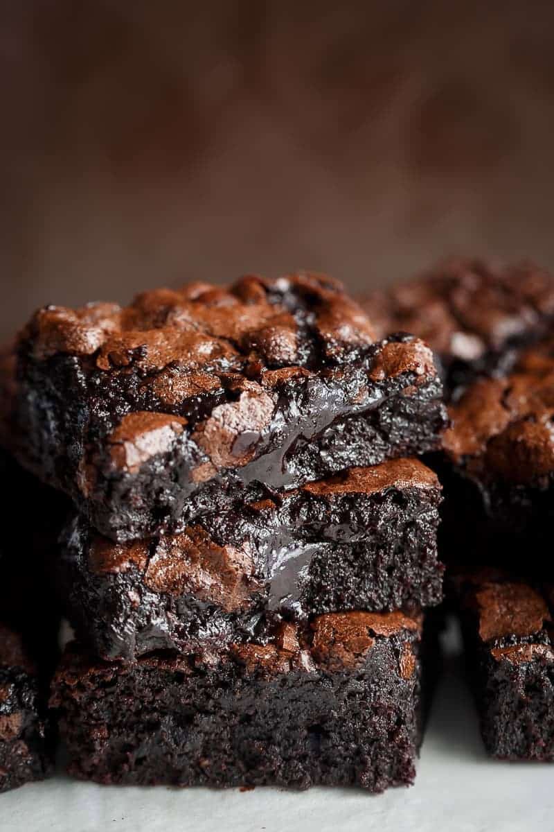 Side view of three slices of chocolate brownie stacked on top of each other. The brownies have a light brown top and dark, gooey interior.