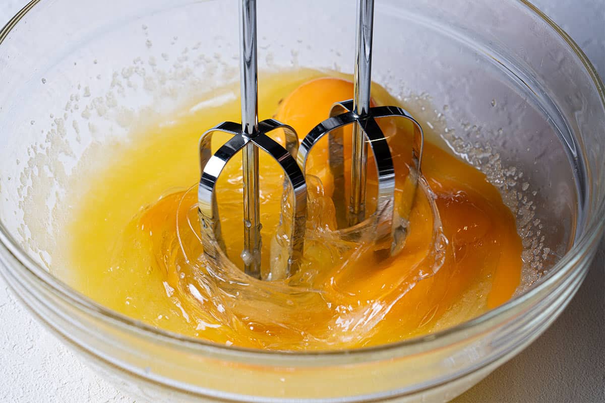 Ingredients being combined with hot melted butter, oil, and sugar in a medium bowl.