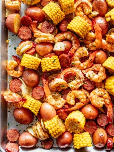 Shrimp Boil smothered in garlic butter mixture and Old Bay seasoning with chunks of red potatoes and corn on the cob on a silver tray.