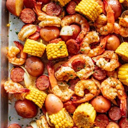 Shrimp Boil smothered in garlic butter mixture and Old Bay seasoning with chunks of red potatoes and corn on the cob on a silver tray.