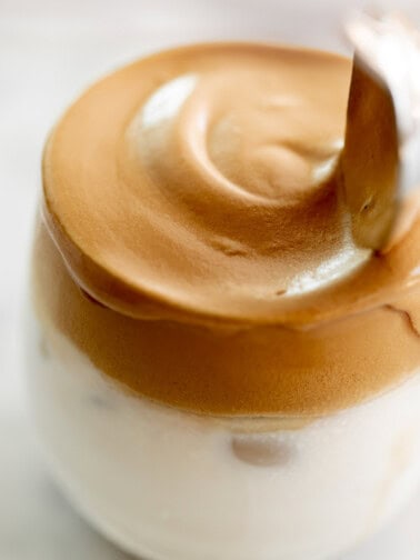 Whipped dalgona coffee on top of a glass full of milk.