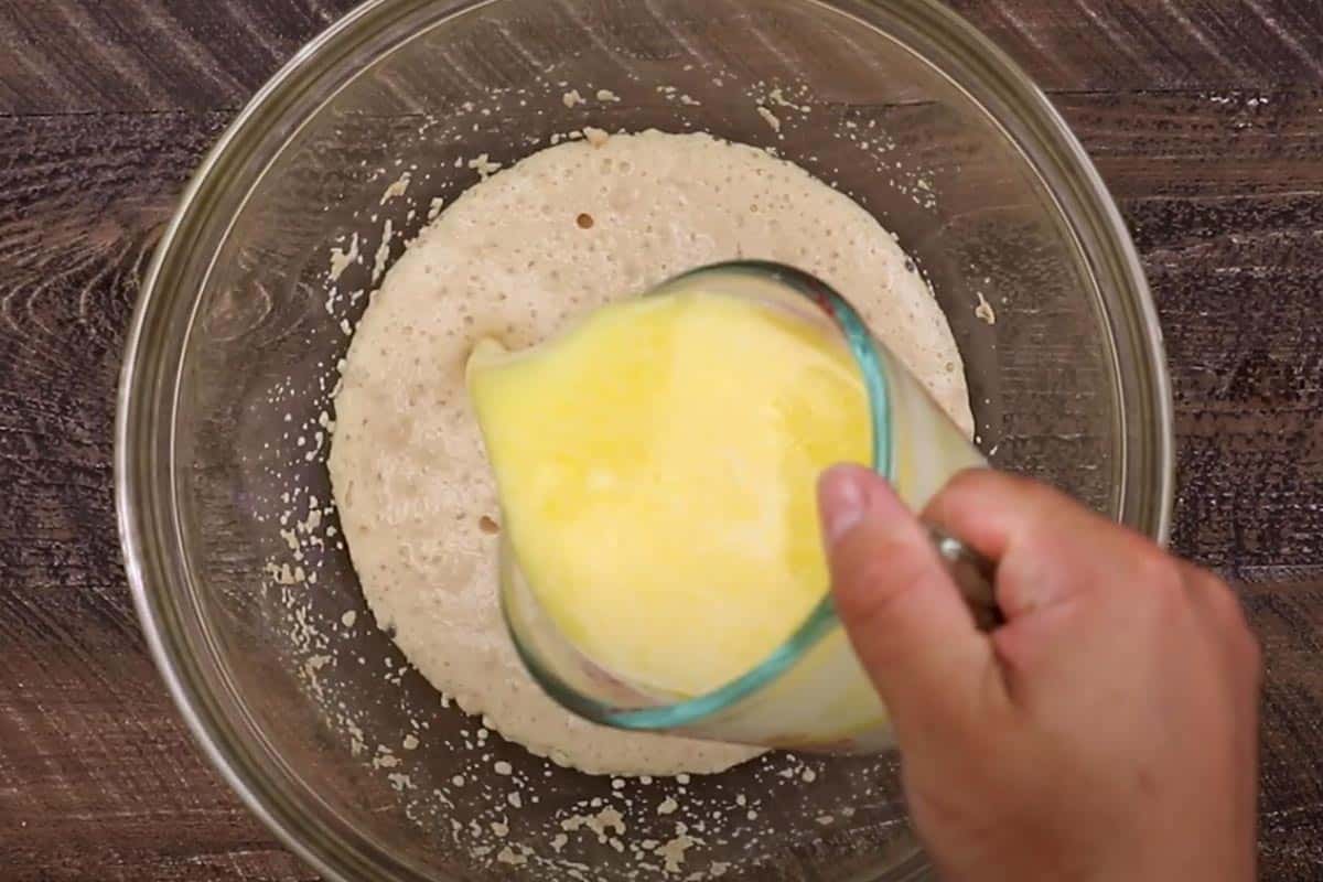 Pouring the mixed milk and butter in the bowl with blooming yeast.