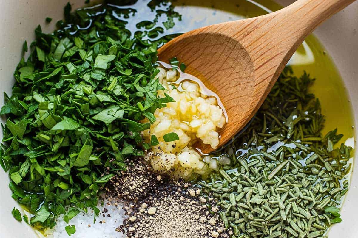 Oil, garlic, parsley, thyme, rosemary, salt, and pepper in a bowl.