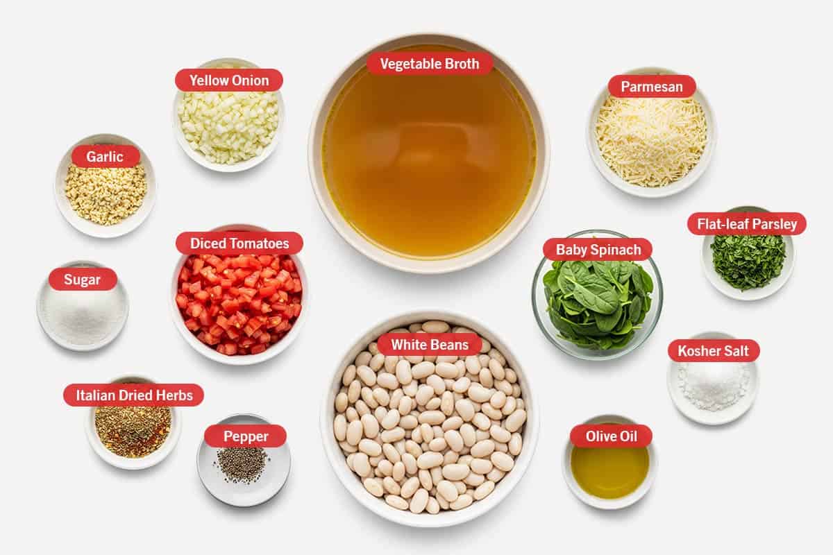 Top shot of ingredients: Vegetable broth, white beans, parmesan cheese, baby spinach, flat-leaf parsley, kosher salt, olive oil, yellow onion, garlic, diced tomatoes, sugar, Italian dried herbs, and pepper.
