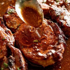 Zoom in image of a silver spoon pouring thin brown sauce over BBQ baked pork chops.