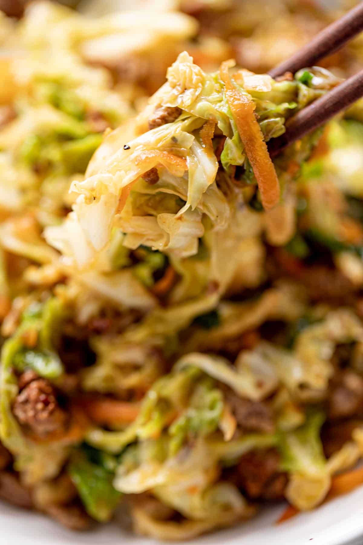 A close up of chopsticks holding cabbage and ground beef.