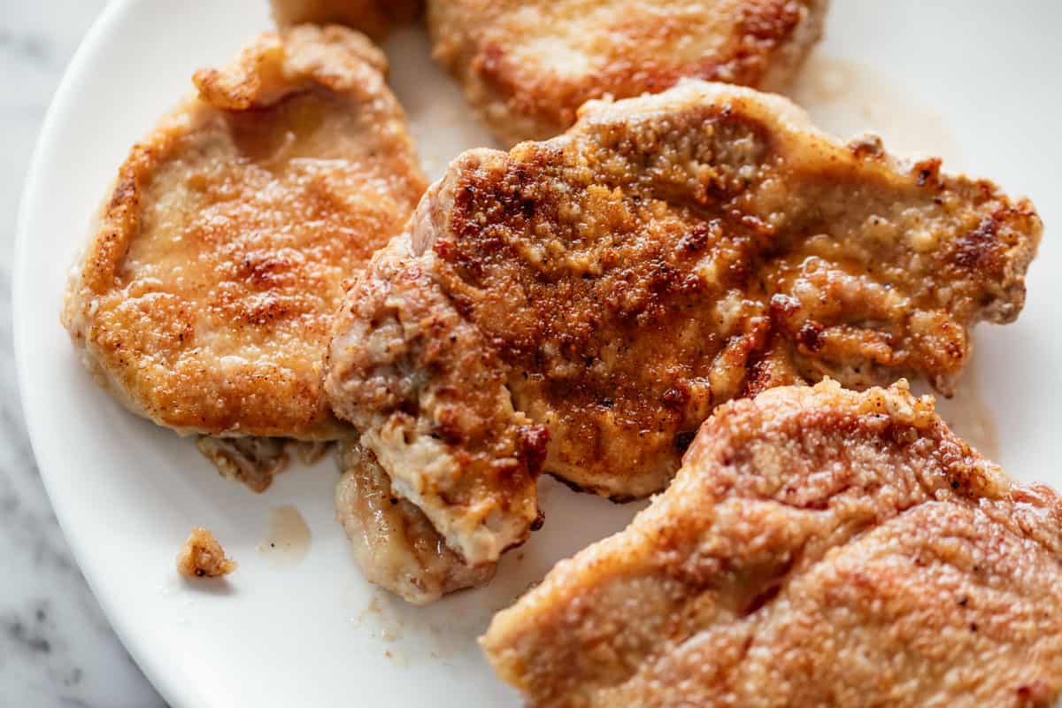 Breaded, seared bone-less pork chops on a white plate.