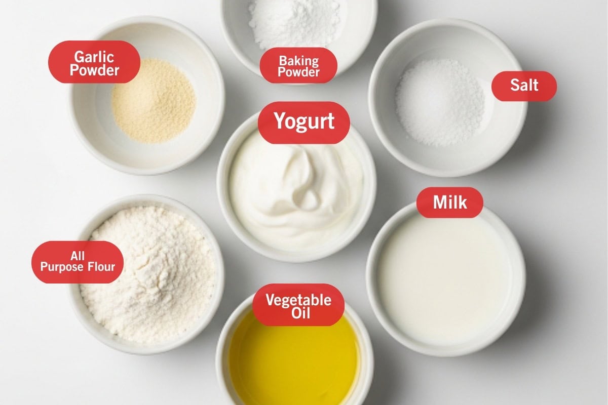 Flay lay photo of ingredient shot of garlic powder, baking powder, yogurt, salt, all purpose flour, vegetable oil and milk