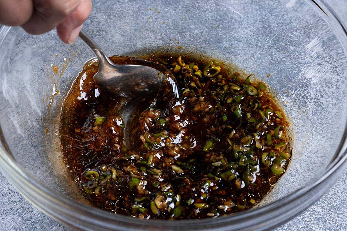 Honey, soy sauce, green onions, cooking oil, garlic, vinegar, sesame oil, and ginger are being mixed together in a clear bowl.