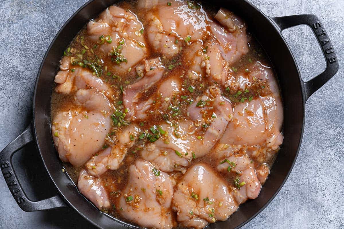 An image of the chicken immersed in the marinade being transferred to the skillet before baking.