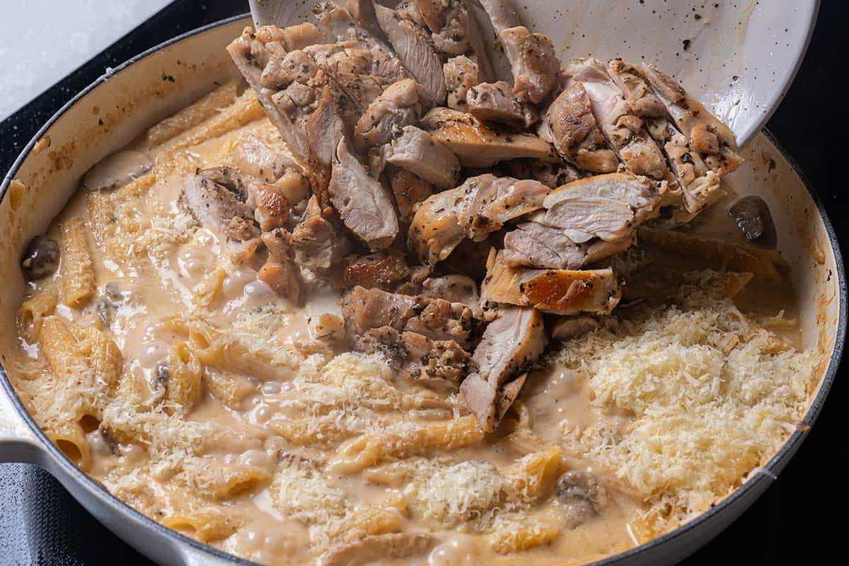 creamy mushroom sauce with penne being poured in with parmesan cheese and chicken thigh