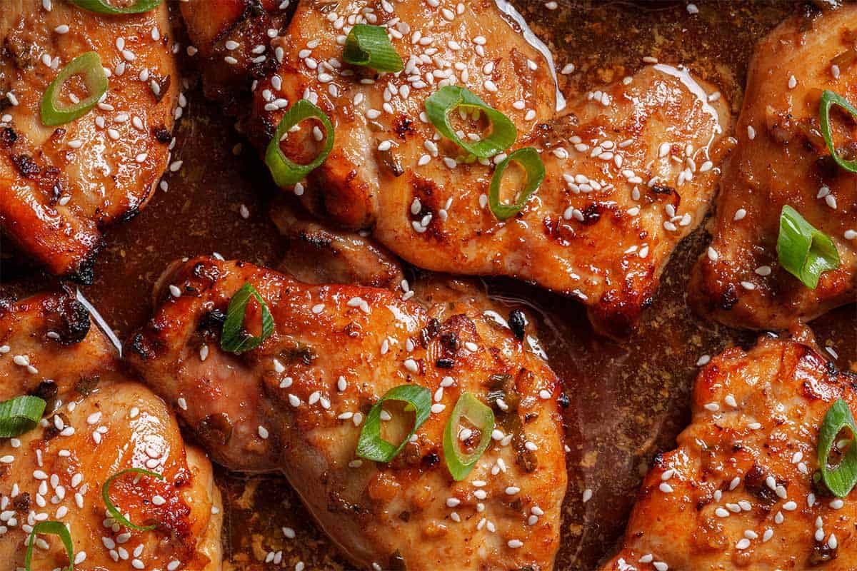 Close-up image of the chicken being taken out of the oven, garnished with sesame seeds and chives.