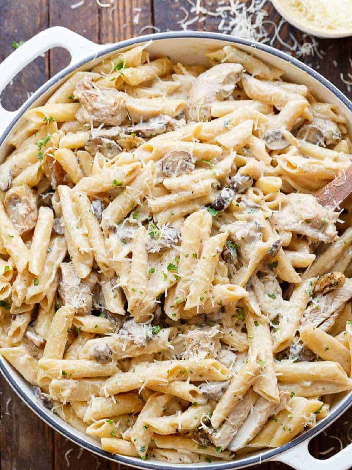 Seared chicken strips mixed through this One-Pot Creamy Mushroom Chicken Pasta, with garlic, mushrooms and parmesan cheese in a large le creuset pot. The pasta is sprinkled with freshly grated parmesan and fresh herbs.