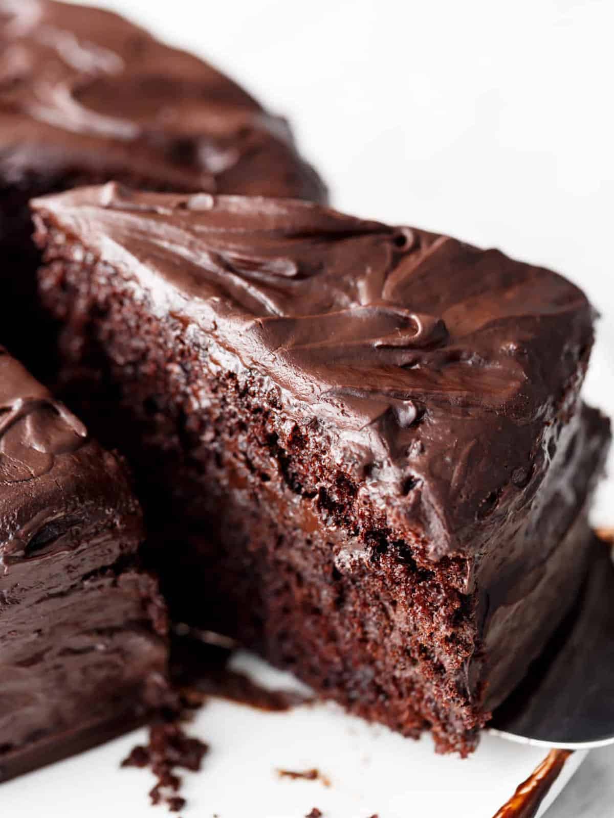 A thick triangle slice of chocolate cake lathered with chocolate butter cream being lifted from the cake with a cake spatula !