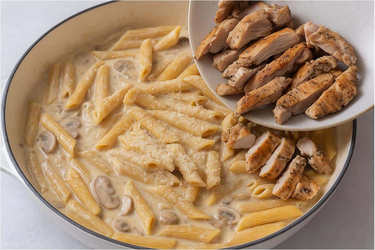 Creamy mushroom sauce with penne being poured in with parmesan cheese and chicken thigh