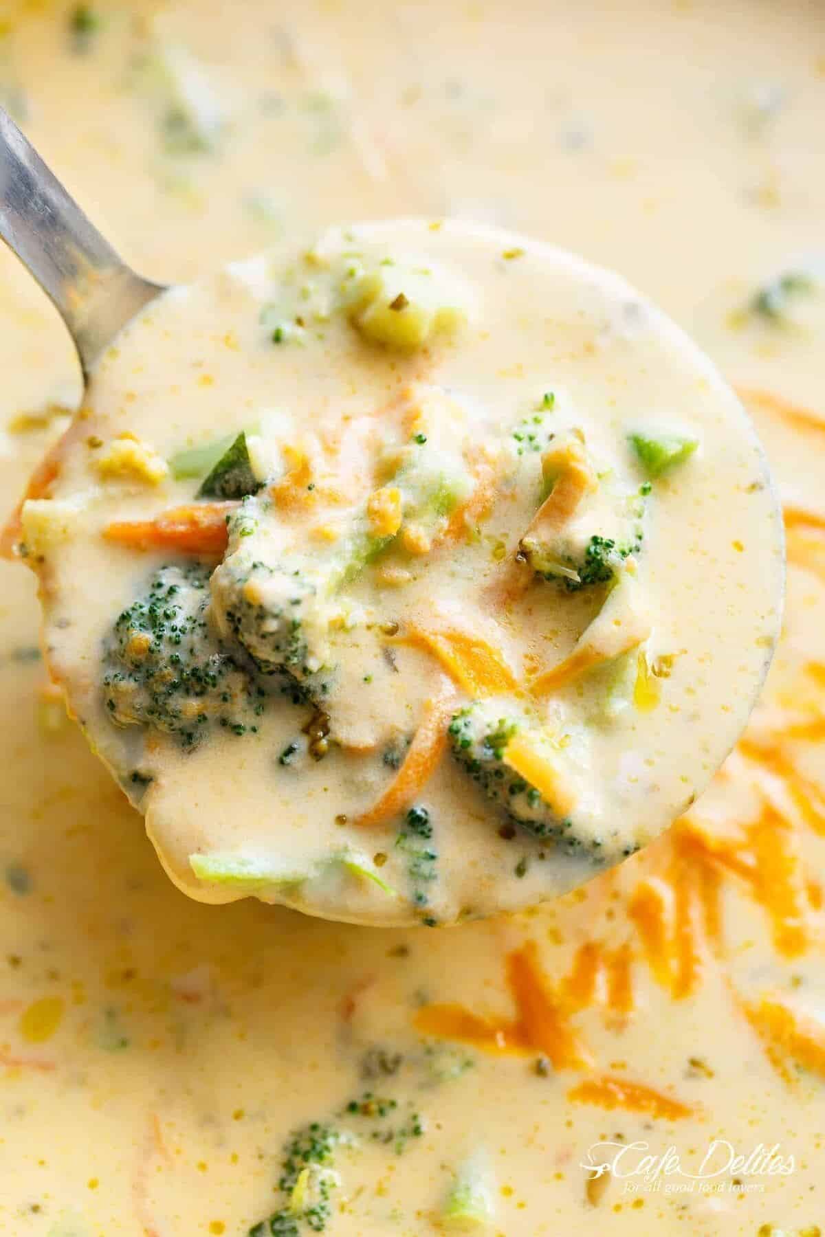 Close up top view of a ladle of broccoli and cheese soup being lifted from a steaming pan