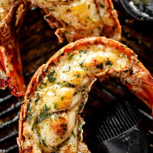 Grilled Lobster Tails garnished with melted garlic herb butter on a black grill pan.